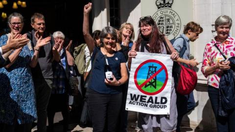 Activists celebrate after a ruling by the Supreme Court holding a sign which reads Weald Action Group 