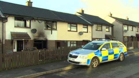 A police car outside the fire-damaged house