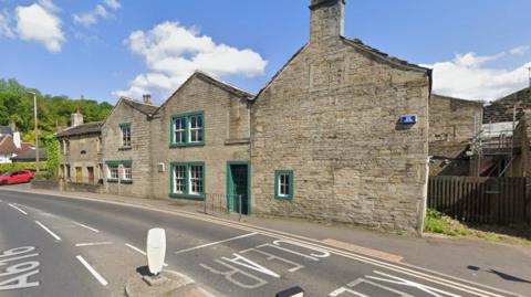 The former White Hart pub in Holmfirth. Pictured is the old pub building, which looks like an ordinary stone house with a green door and window frames.