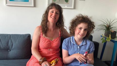 A mum in a red dress and a young child in her school uniform