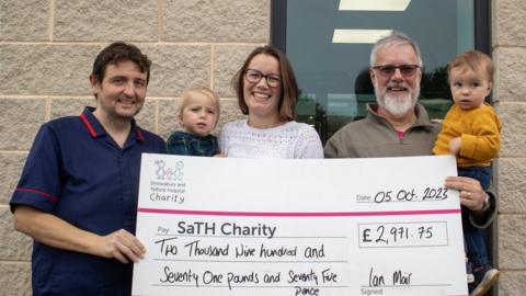 Ian Mair, his daughter Kathryn and his grandchildren present a large cheque to ward manager Peter Warren