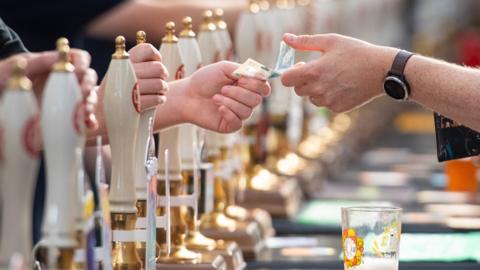 Row of beer pumps in a bar with bar staff taking money from customer