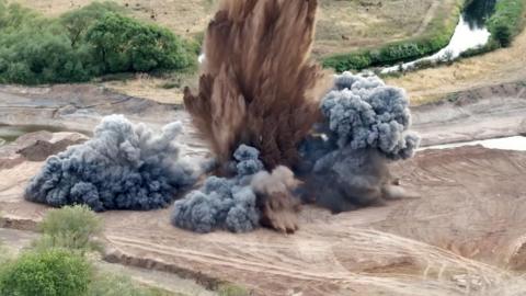 Smoke and dirt explode into the air on a site filled with sand and grass.