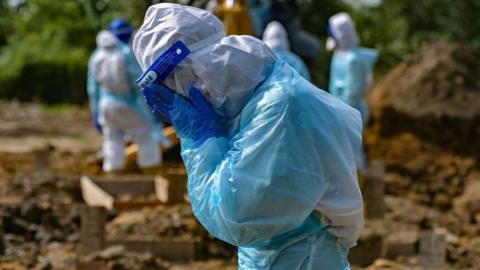 A family member wearing personal protective equipment reacts during the burial of his relative who died fighting the Covid-19 coronavirus in Klang, Malaysia