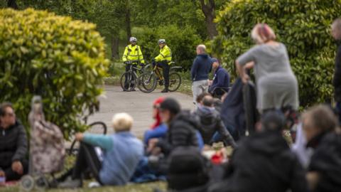 Police officers look-on as members of the public attend a gathering in May 2020 in Greenfield