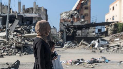 A woman and girl walk past destroyed residential buildings in Al Nuseirat refugee camp