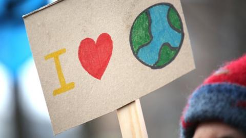 A person holding an illustrated sign that reads: I love the world