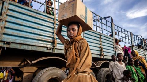 A Sudanese girl who have fled from the war in Sudan with her family carry a box with some of her belongings after arriving at a Transit Centre for refugees in Renk, on February 13, 2024