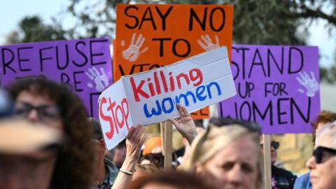 People hold signs at a rally to call for action to end violence against women, in Canberra, Australia 28 April 2024.
