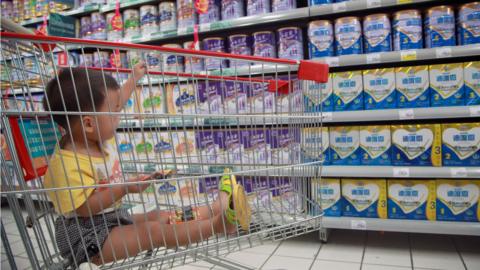 A baby stays in a shopping cart as his mother selects baby milk in a supermarket in Haikou, south China's Hainan province