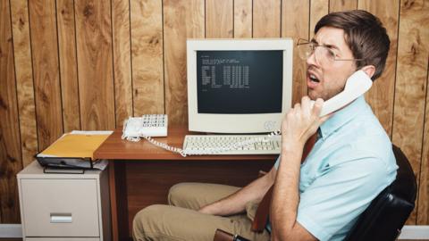 A 1990s office worker sits at his desk on the phone