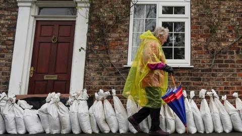 A woman walks past sand bag flood defences in the village of Naburn near York as water levels rise on the River Ouse.