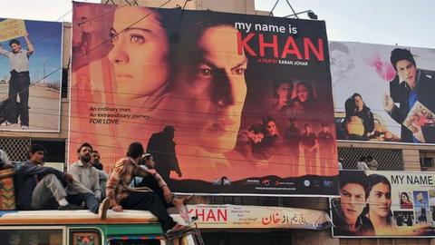 Pakistani commuters, sitting on top of a bus, pass by a cinema screening Indian Bollywood actor Shah Rukh Khan's film 'My Name is Khan' in Karachi on February 12, 2010.