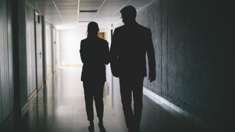 Woman in silhouette talking to man in a corridor