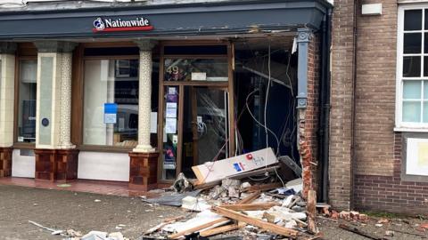 front of store smashed with bricks, glass and wood across the pavement.