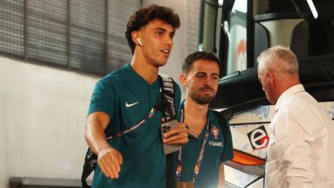 Joao Felix pictured getting off a coach while on international duty with Portugal. He is smiling and earing headphones, with international team-mate Bernardo Silva of Manchester City just behind him.