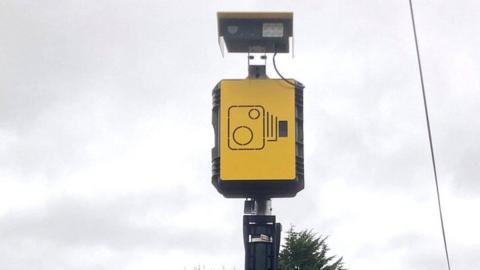 An automatic number plate recognition camera on a pole against a cloudy sky