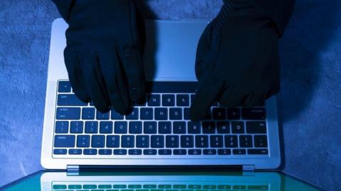 Stock photo of gloved hacker using computer