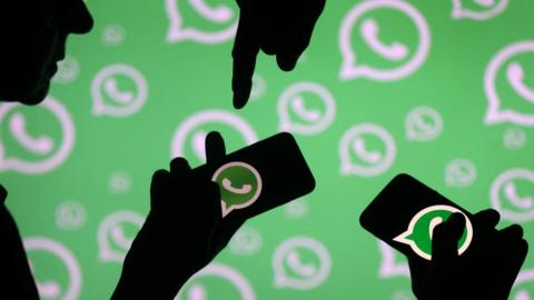 Men pose with smartphones in front of displayed Whatsapp logo.