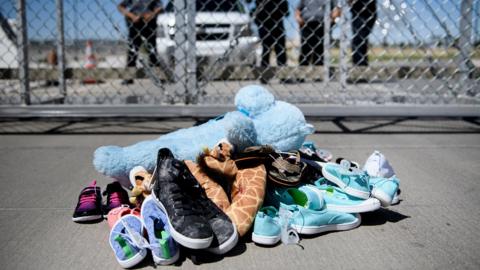 Shoes and toys left at the Tornillo Port of Entry with security personnel in the background as part of a protest in Tornillo, Texas (21 June 2018)