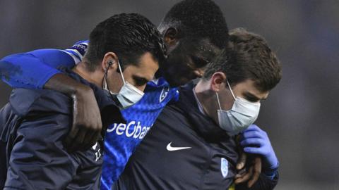 Nigeria striker Paul Onuachu (centre) led off the pitch by Genk's medical team