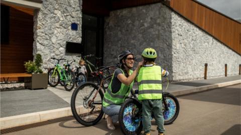 Young woman wearing cycling helmet and waistcoat and preparing her son for bike riding