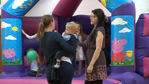 Mother holding baby in front of a bouncy castle