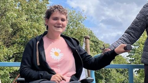 A teenage girl with short brown hair, holding onto a rail. She is smiling.