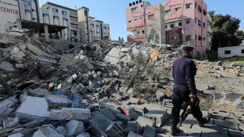 Hamas policeman walks past the remains of a building in Gaza City destroyed in an Israeli air strike (26 March 2019)