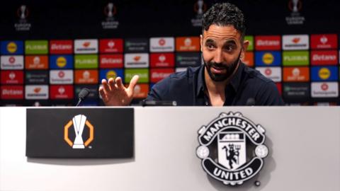 Ruben Amorim speaks in front of a white desk with the Manchester United logo during a press conference