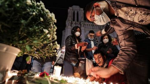 People lights candle outside the Notre-Dame de l'Assomption Basilica in Nice on October 29, 2020