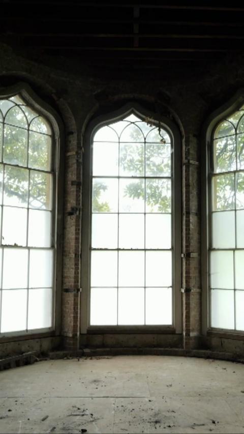 Large and tall windows are pictured in an historic mansion, with bright indirect light beaming through. The floor is dirty and dusty.