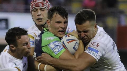 Louis Senior for Huddersfield, flanked by Catalans tacklers