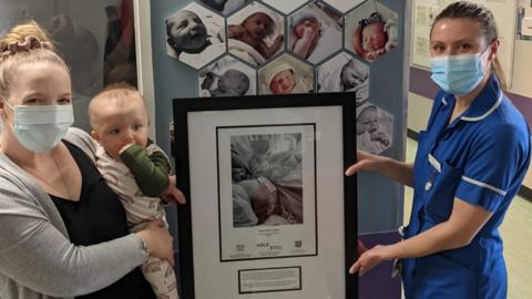 Ali Harris holding baby Indy while handing over a framed photo to a nurse