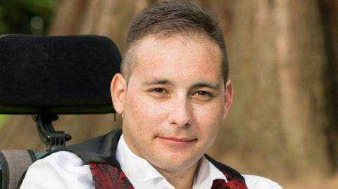 Karl Lee wearing a white shirt and red, printed waistcoat.