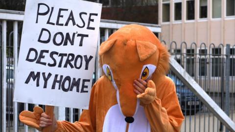 A person in a fox costume holding a sign