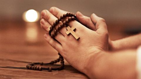 A person clasps their hands together, holding a rosary