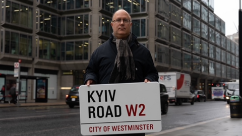 Councillor Adam Hug holds up a Kyiv Road sign