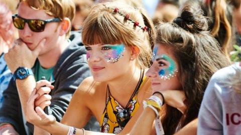 Female festival goers in a crowd wearing glitter on their faces.