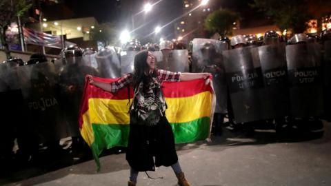 A woman stands in front of police