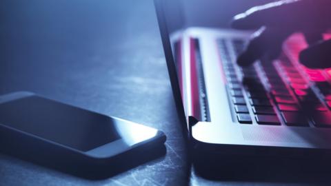 Close up of a hand on a laptop next to a phone