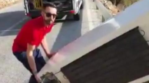 Man about to throw fridge off ravine looks directly at the camera