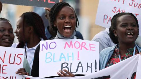 A woman holds up a sign that says 'no more blah! blah!'
