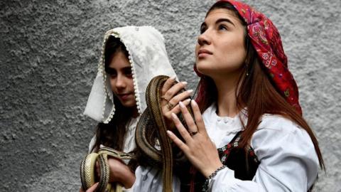 Faithfuls in traditional clothing hold snakes to place them on the statue of Saint Domenico during an annual procession in the streets of Cocullo