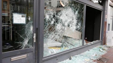 shop window riddled with holes, broken glass on the ground