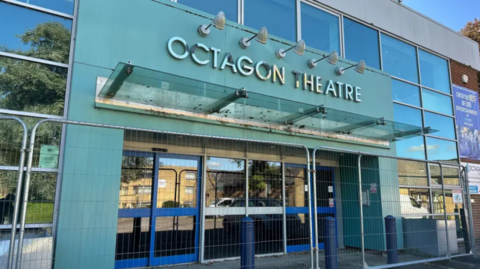 A recent photograph of what the Octagon Theatre looks like focusing on the main entrance. There is fencing preventing entry.