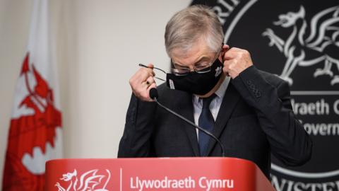 Mark Drakeford puts on a face mask during the Covid-19 lockdown