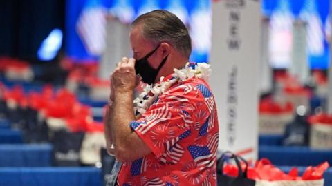 A delegate wears a mask and a Hawaiian flag covered in US flags