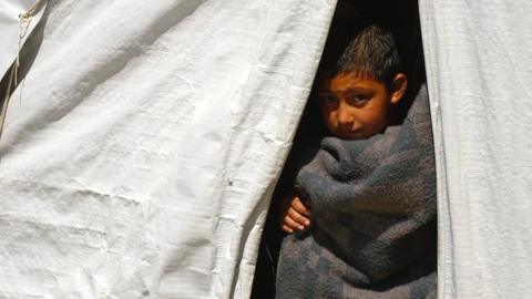 A child covered in a blanket peers out of a tent