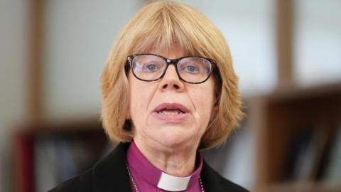 Dame Sarah Mullally, who has a blonde bob hairstyle with a fringe and wears glasses with a dark frame, is pictured speaking at a previous event at Chapter House in Canterbury Cathedral